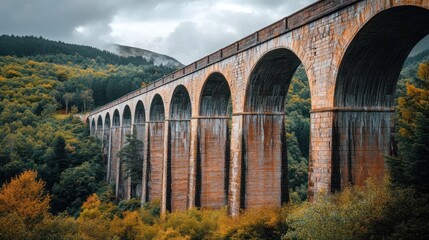 Aged stone railway viaduct arches spanning a valley with colorful autumn foliage.