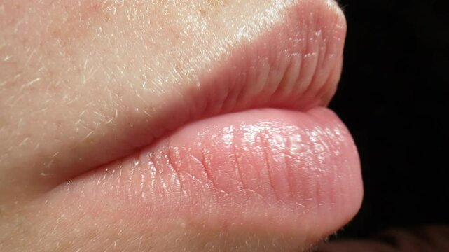 Macro close-up of human lips slightly parted, revealing teeth while speaking. Girl is speaking in slow motion macro. Texture of the lips, surrounding skin, emphasizing communication and expression