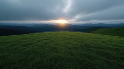 Obraz premium Lush green meadow atop a mountain range at sunset. Dramatic clouds and sunlight break through the stormy sky