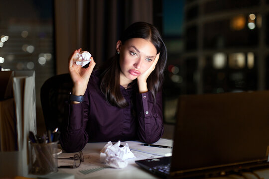 Tired young businesswoman crumple document and looking at laptop screen, working late in office. Entrepreneur overwork at night