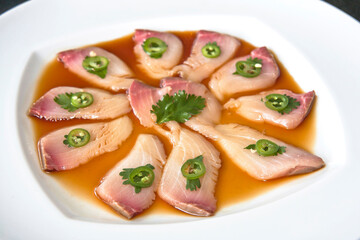 Yellowtail sashimi with jalapeño and soy sauce on a white plate, close-up of raw yellowtail sashimi