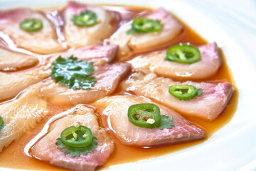 Yellowtail sashimi with jalapeño and soy sauce on a white plate, close-up of raw yellowtail sashimi