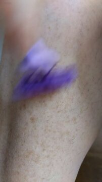Un primer plano de la mano de una mujer afeit&aacute;ndose una  pierna  con bastante pelos y pecas. Video Vertical.