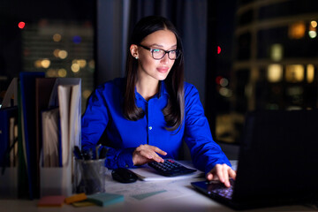 Young woman accountant using calculator, working with laptop and documents at her desk in modern...
