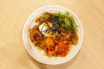 Delicious rice bowl topped with grilled pork, kimchi, a soft-boiled egg, sliced green onions, shredded seaweed, and sesame seeds, served with a flavorful sauce