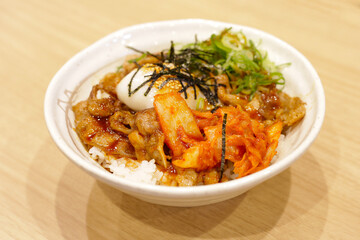 Delicious rice bowl topped with grilled pork, kimchi, a soft-boiled egg, sliced green onions, shredded seaweed, and sesame seeds, served with a flavorful sauce