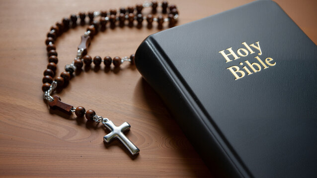 A Holy Bible with a wooden rosary placed on a wooden table, symbolizing faith