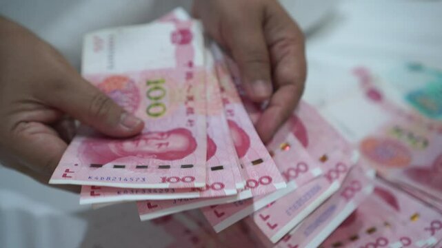 China's economy, Renminbi in global finance or world trade. Counting yuan banknotes Chinese currency (Renminbi or RMB) featuring 100-yuan banknote with Mao Zedong's portrait