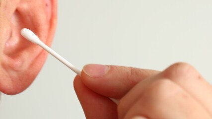 a person is cleaning their ear with a cotton swab against a light background.