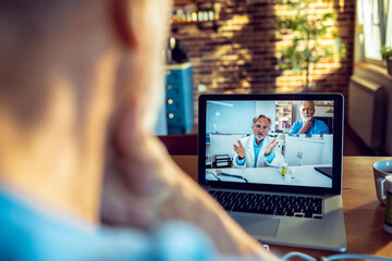 Fototapeta premium Senior man having a video call with his doctor on the laptop while having breakfast in the morning