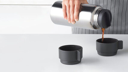 Closeup of a person filling two plastic cups with coffee.