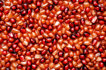 Vibrant pomegranate seeds are closely photographed, displaying a rich texture and a mix of deep red and bright orange colors. A healthy and natural food component.