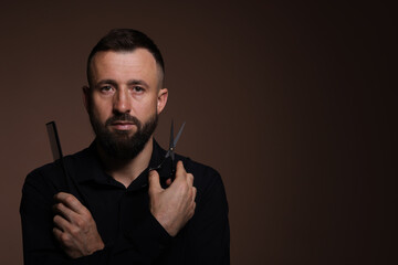Bearded man holding comb and scissors on brown background, space for text