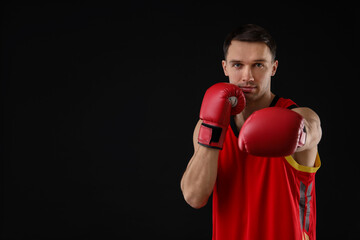 Man in boxing gloves fighting on black background, space for text