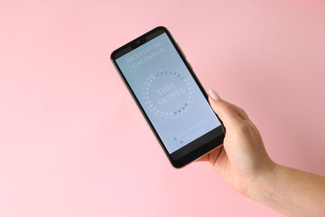 Menstruation. Woman holding smartphone with period calendar application on pink background, above view