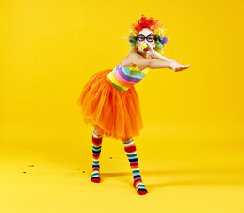 Girl dressed like clown with blowers on yellow background. Surprise party
