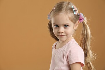 Cute little girl wearing beautiful hair accessories on light brown background. Space for text