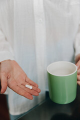 Woman holding white pill next to cup of coffee on table