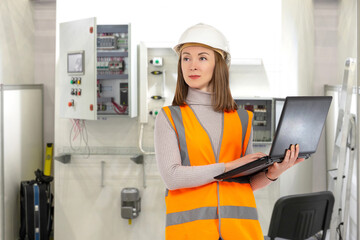 Woman electrical engineer. Girl with laptop near power shields. Electrical cabinets behind...