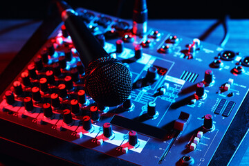 Professional mixing console with microphone on table in neon lights, closeup