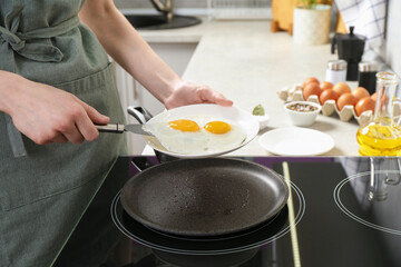 Woman putting tasty fried eggs onto plate in kitchen, closeup