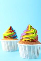 Delicious cupcakes with colorful cream on light blue background, closeup