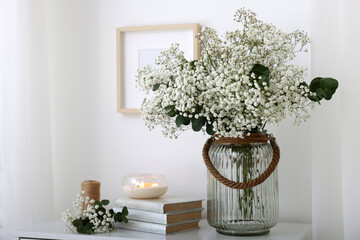 Bouquet of beautiful gypsophila flowers and eucalyptus branches in vase near decorative elements on chest of drawers indoors