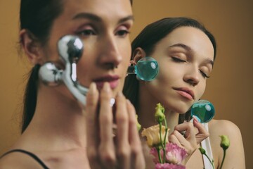 Women using facial rollers while surrounded by flowers in a serene setting