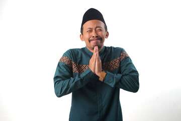 Asian Muslim man crying with a sorrowful expression, hands clasped together as he begs for...