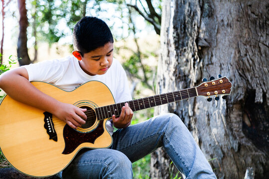 Boy playing country music on acoustic guitar in bushland
