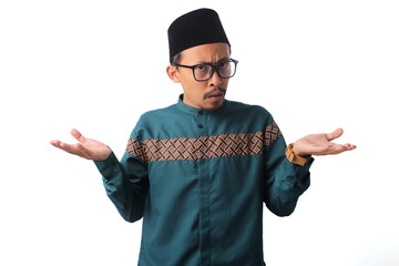 Clueless and unaware Asian Muslim man spreading his palms in doubt, expressing uncertainty with a hesitant expression, and shrugging his shoulders, isolated on a white background.