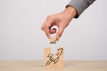 Close-up of a hand placing a final puzzle piece illustrating a rocket, symbolizing business growth,...
