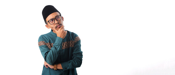 Thoughtful Asian Muslim man resting his hand on his chin, gazing away at empty copy space while thinking, isolated on a white background
