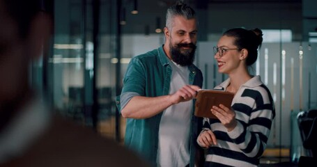 Male senior coach or speaker sharing business ideas and collaborating with a diverse team in a modern office, presenting a project on a tablet during a brainstorming session in a startup hallway - Powered by Adobe