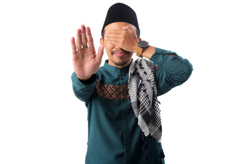 Asian Muslim man covers his eyes while showing a stop gesture, symbolizing self-discipline in...