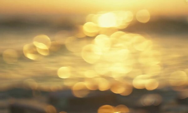 Abstract sea summer ocean sunset nature background. Small waves on golden water surface in motion blur with golden bokeh lights from sun. Holiday, vacation and recreational concept. Nobody Slow motion