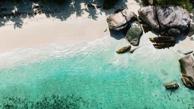 Large rock formations by the turquoise water of a tropical beach, surrounded by green foliage. Seychelles, Mahe. Roche Copra.