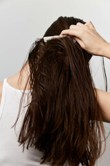 Naklejka premium Hair grooming, woman with wet dark hair, combing hair, natural beauty, self care, casual appearance, profile view, indoor setting, minimalist background