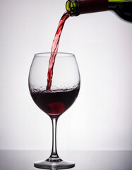 Pouring tasty red wine in glass on white background, closeup. Space for text