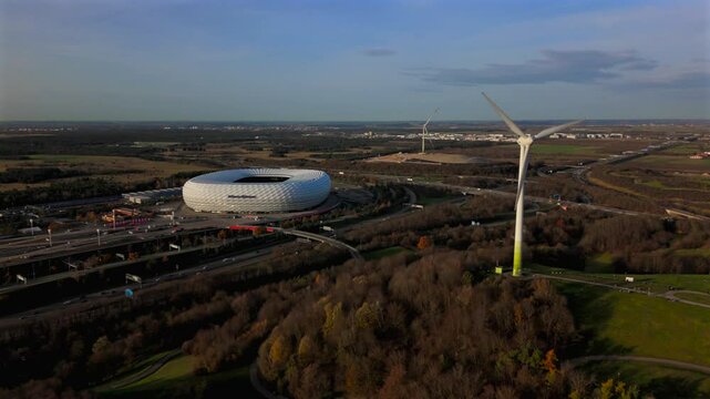 Aerial view of the Froettmaninger Hill with a wind turbine and a scenic view of the Allianz Arena in Munich. Freimann wind power plant and Munich football arena captured from above. 