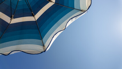 White and shades of blue striped beach umbrellas. View from below. Blue sky. Relaxing context. Summer holidays at the sea. General contest and location