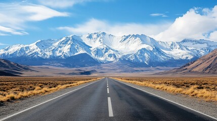 Naklejka premium Scenic highway stretches towards majestic snow-capped mountains under blue sky
