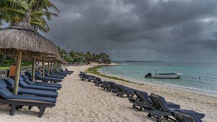 A row of deck chairs with mattresses under straw umbrellas on a sandy beach. Footprints in the...