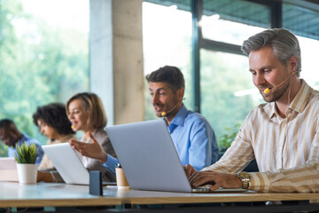 Obraz premium Portrait of call center worker accompanied by his team. Smiling customer support operator at work.