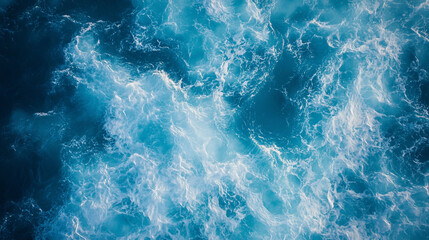 Aerial view of ocean water with white foam creating a dynamic and textured surface pattern in blue tones.