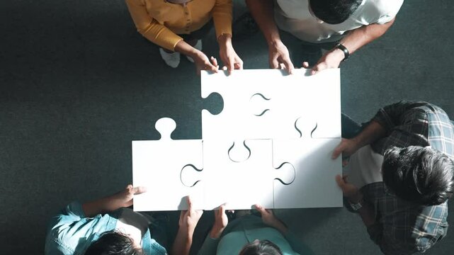 Top down view of business people put last piece of jigsaw puzzle together to complete puzzle and standing while wearing casual cloth. Group of diverse team finding solution with teamwork. Symposium.