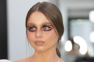 woman with long brown hair and blue eyes is wearing a necklace with pearls. She has blue eyeliner...