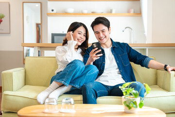 Young couple enjoys content together at home laughing and smiling while looking at a mobile phone