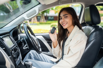 Naklejka premium Young beautiful asian business women in suit getting new car showing car key. she very happy and excited in hand holding car key. Smiling female driving vehicle on the road city on a bright day