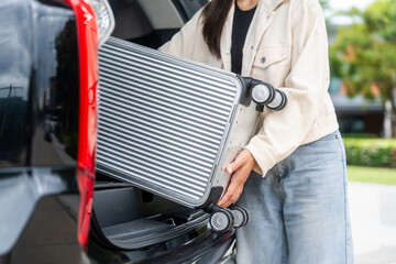 Young woman puts her suitcase in the back of the car and prepares to travel trip. Open the back of...